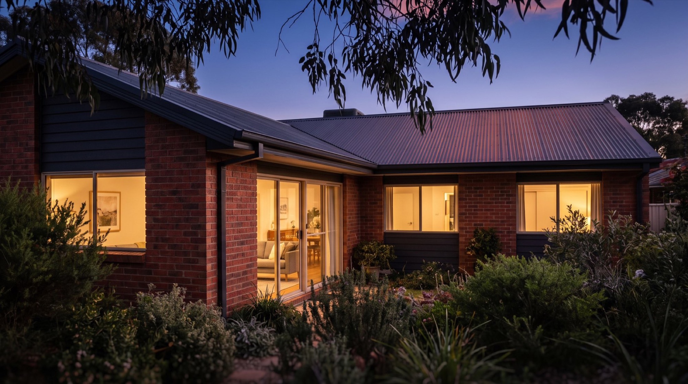 A low-set home at dusk with warm light in the windows