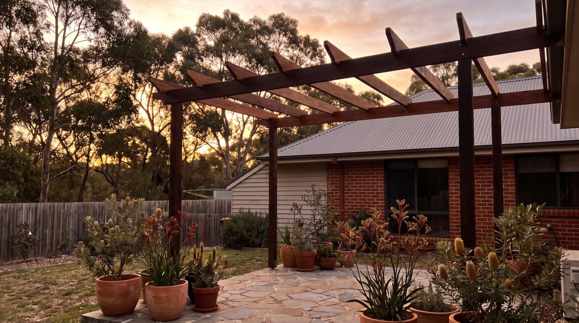 A timber pergola over a garden path beside a home at dusk