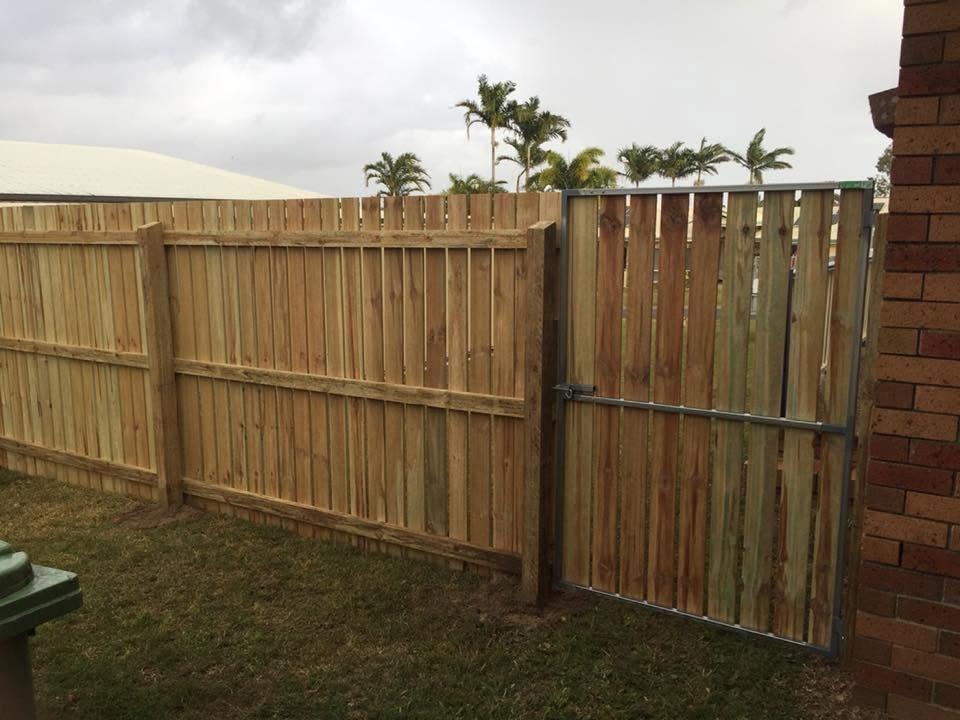 A timber paling fence returning into a brick pier beside a lawn