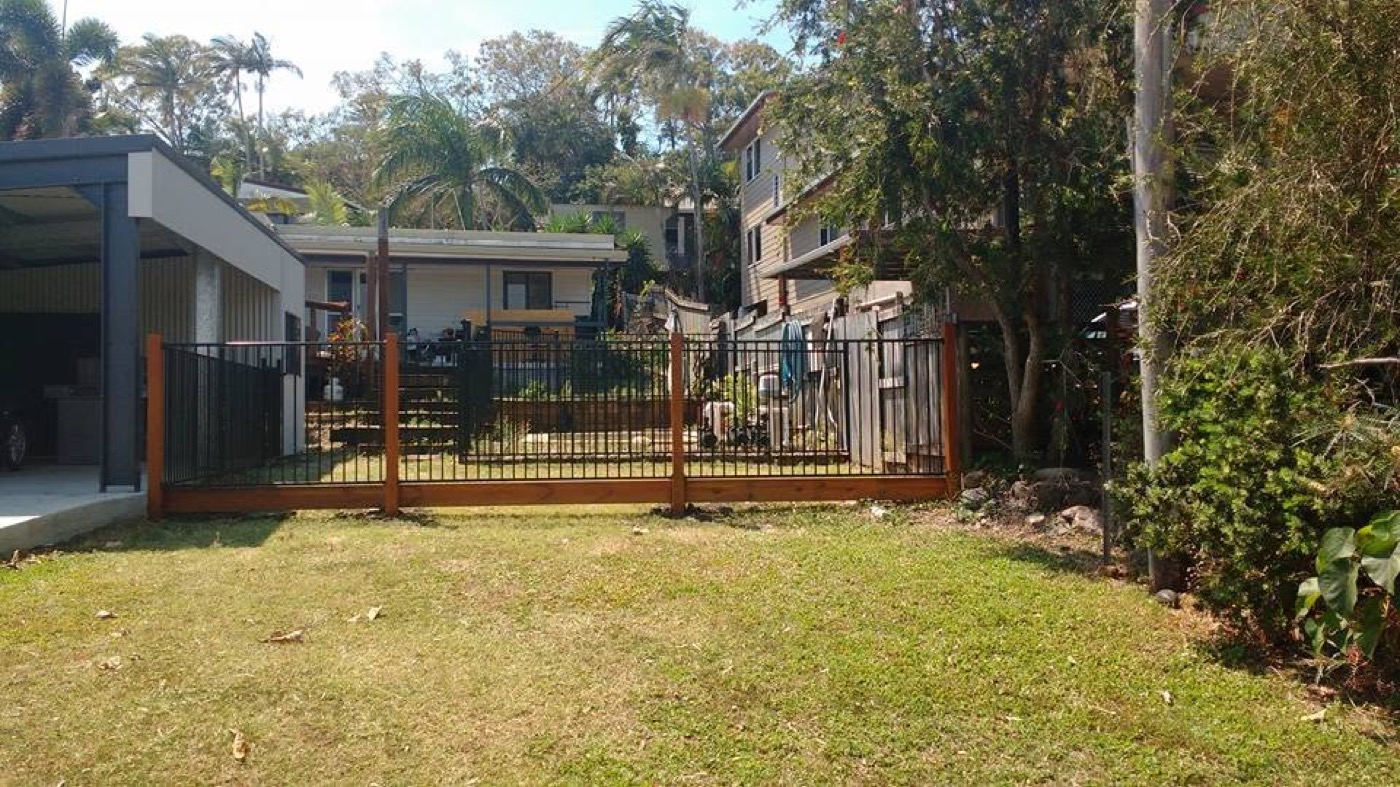 A mown backyard enclosed by a timber fence with palms behind