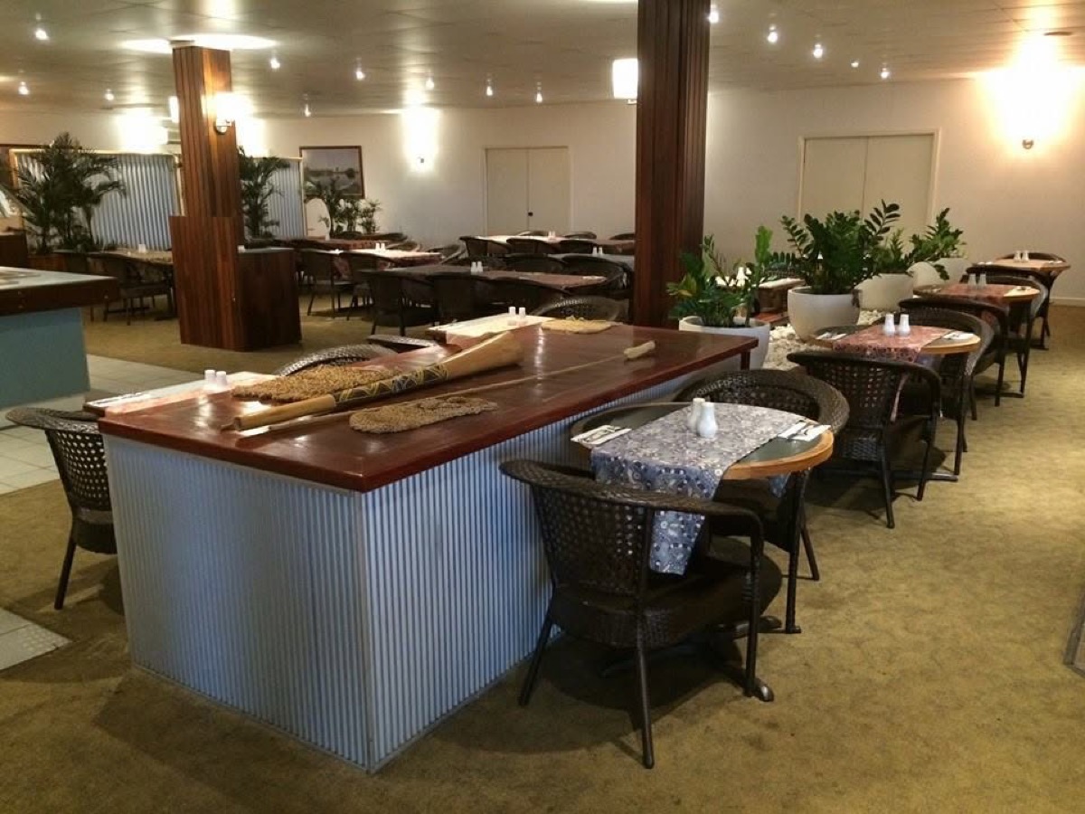 A dining room in a venue with timber tables, cane chairs and a servery bar