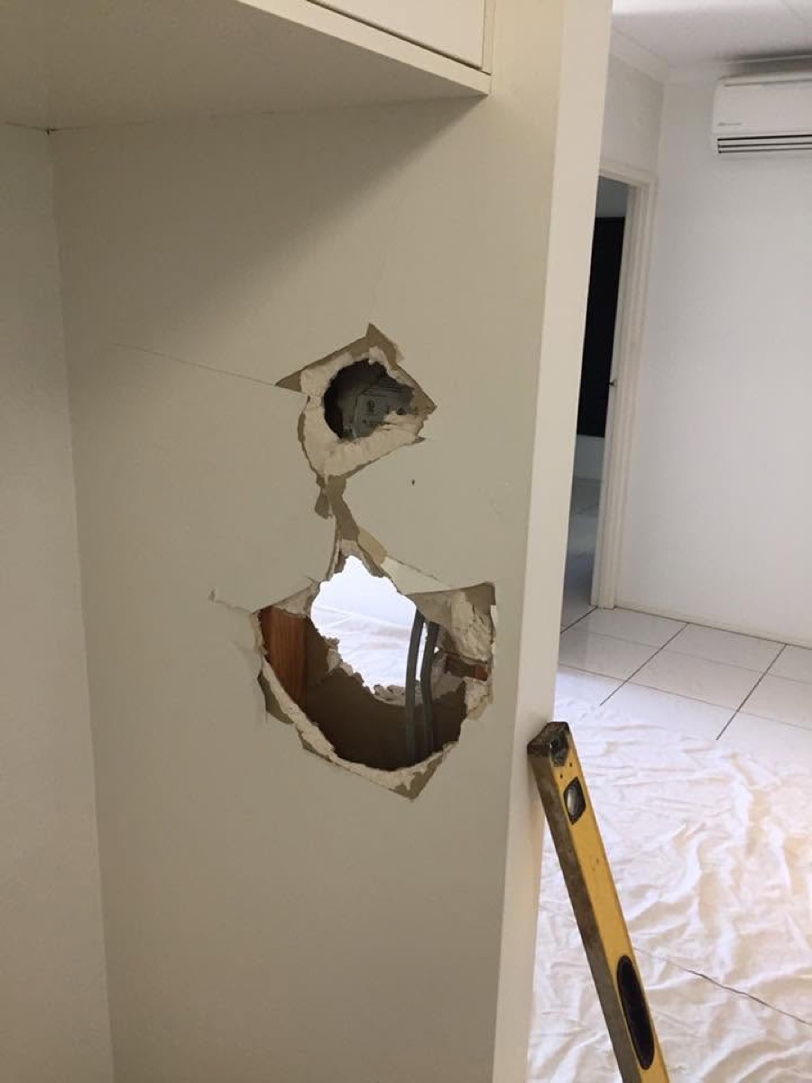 A hole opened up in a plasterboard wall with a level and a drop sheet below