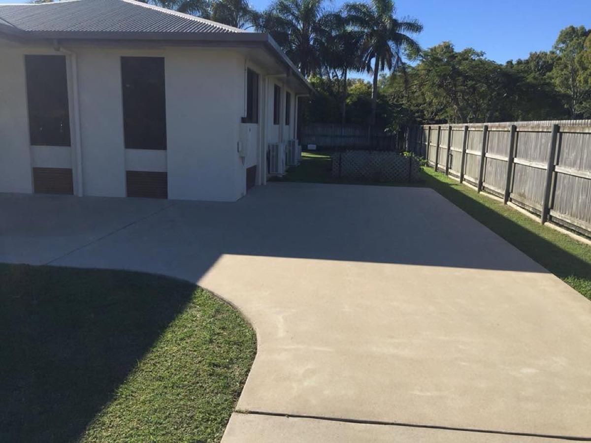 A wide concrete driveway running past a rendered home with palms behind