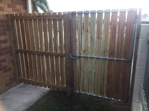 A timber gate hung on a steel frame between a fence and a block wall