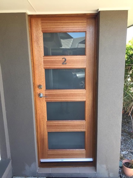 A timber front door with four glass panels fitted to a rendered entry