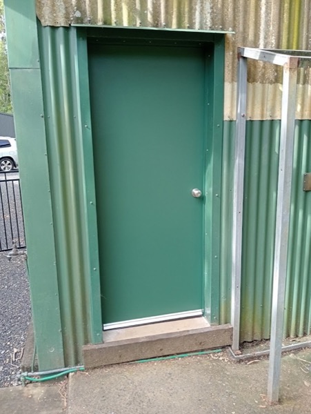 A green painted door fitted into a colorbond shed wall