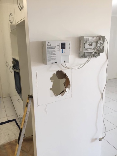 A wall opening cut around conduit beside a mounted control box