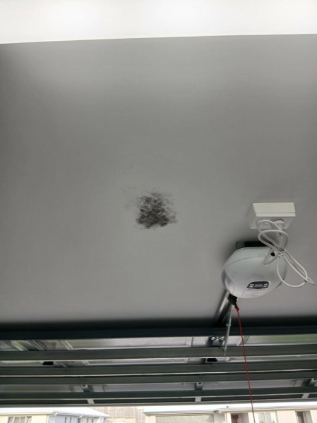 A patched section of ceiling in a garage beside the roller door motor