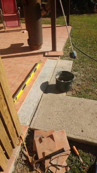 A concrete step poured beside a tiled patio with a level resting on it