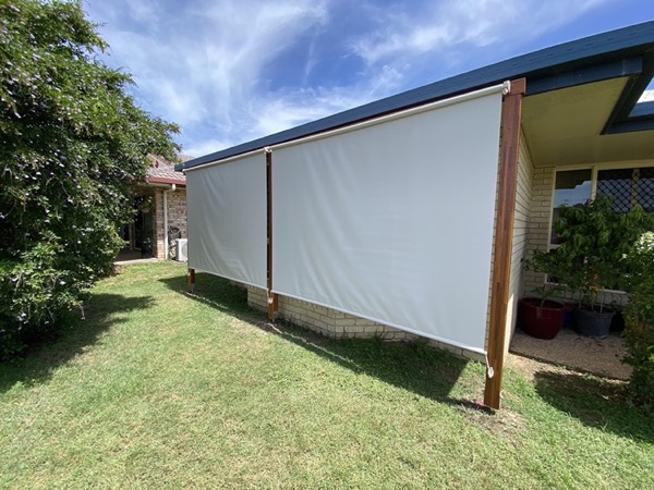 A shade blind hung along the side of a house on timber posts