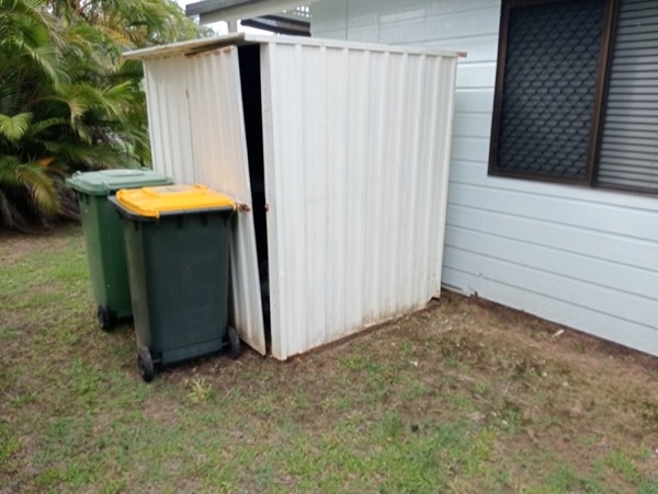 A garden shed standing beside a house with wheelie bins alongside