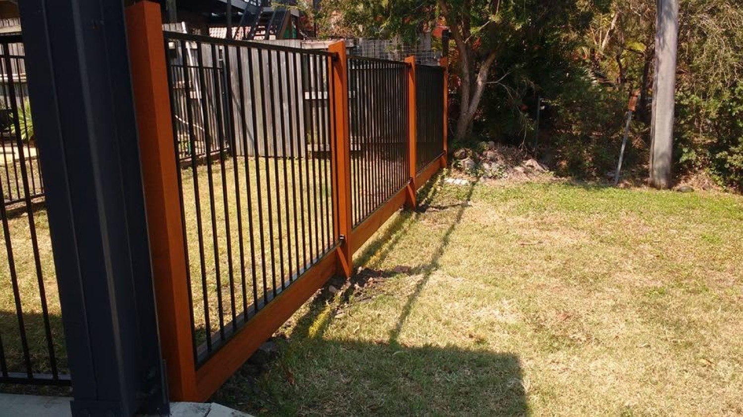 An aluminium fence with timber posts running across a back lawn