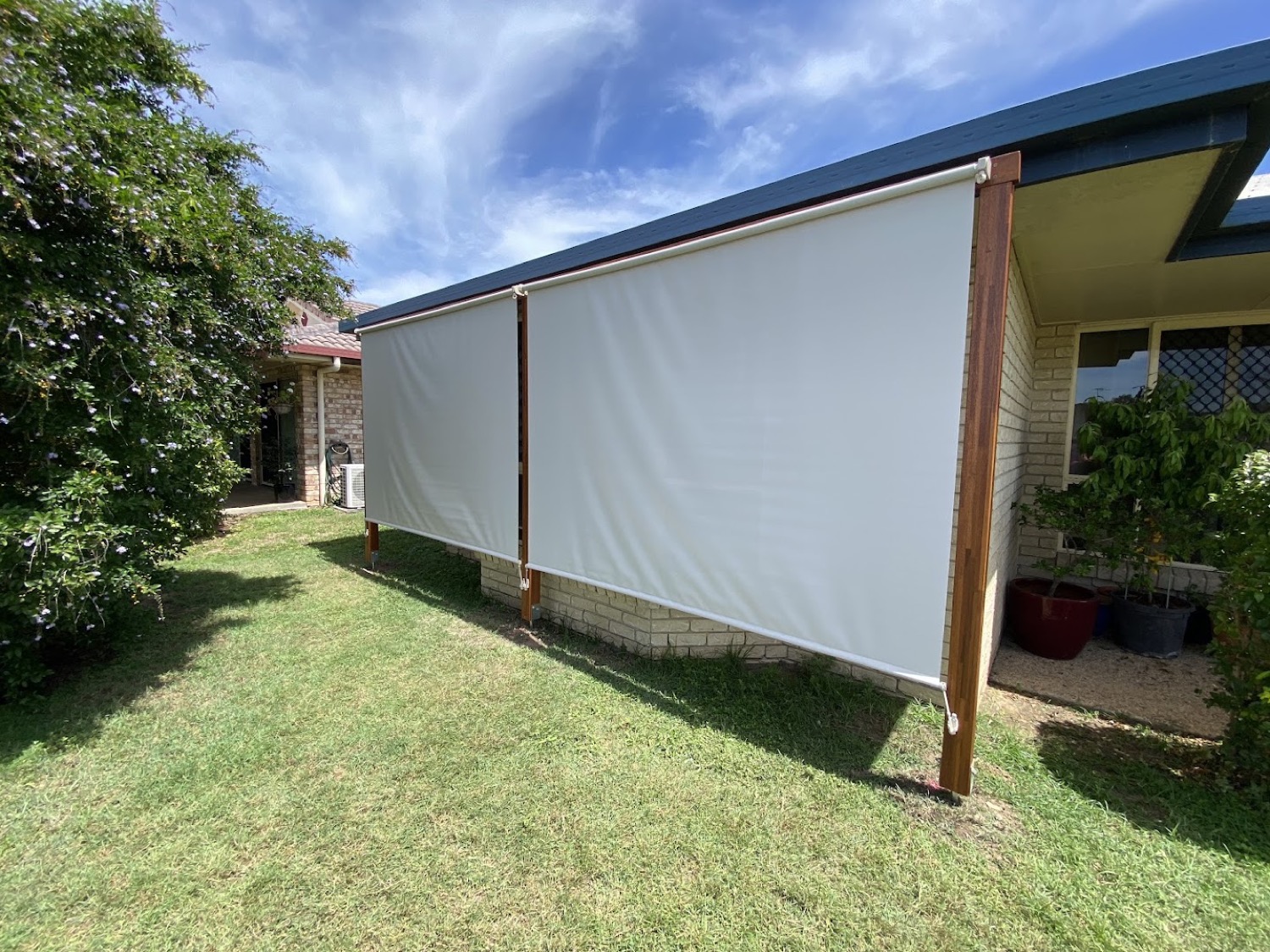 A shade blind hung along the side of a house on timber posts